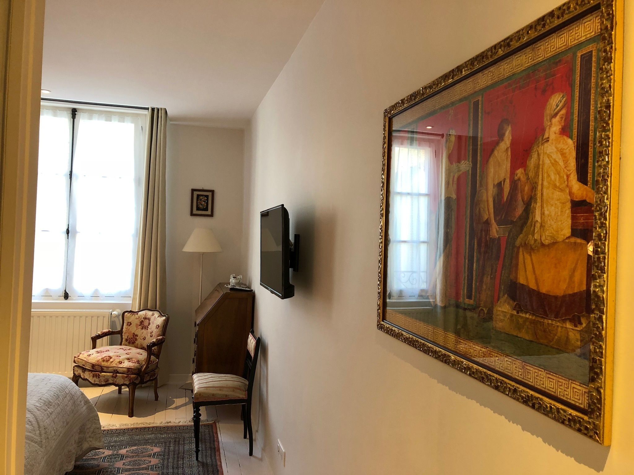 A hotel room with a large painting, a television, a chair, and a bed.