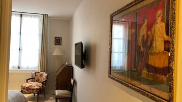 A hotel room with a large painting, a television, a chair, and a bed.