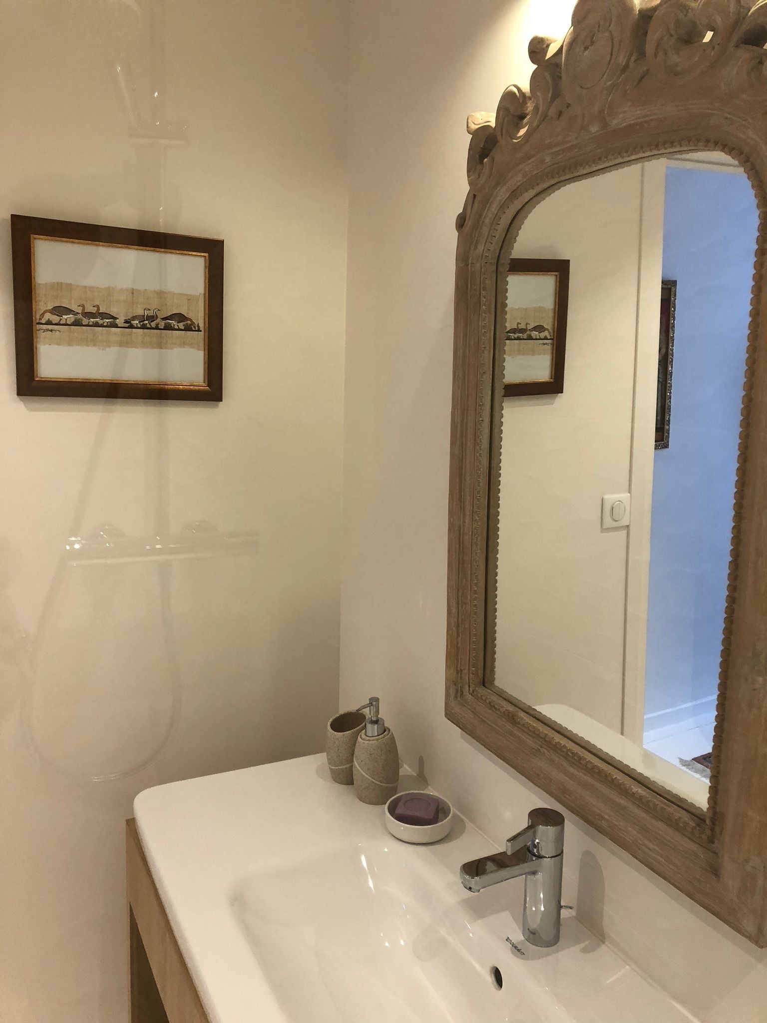 Une salle de bain avec un lavabo blanc, un grand miroir et un tableau encadré accroché au mur.