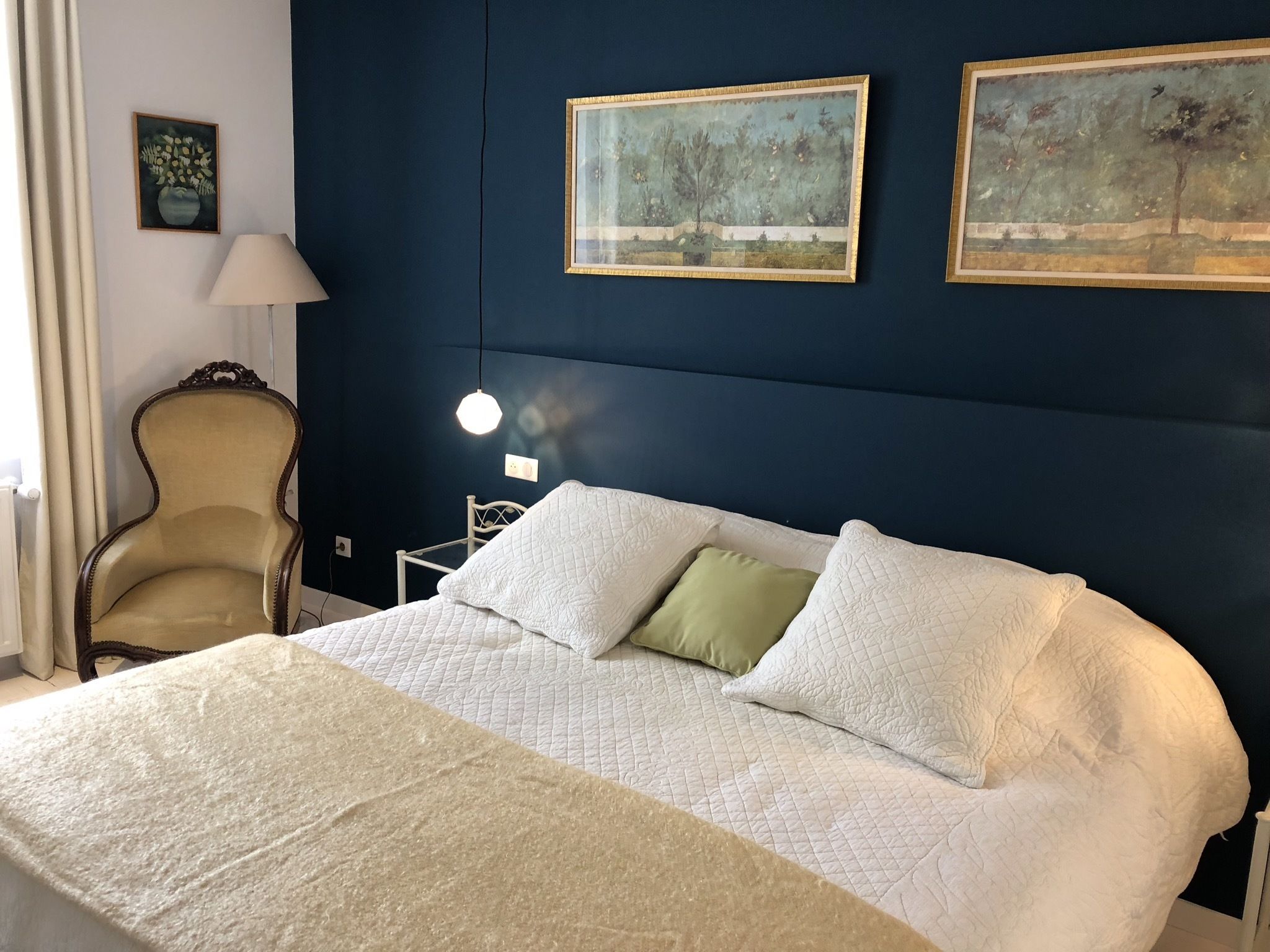 Un dormitorio con cama, una silla y dos cuadros en la pared.