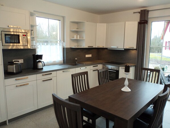 A modern kitchen with white cabinets, a microwave, a coffee maker, and a dining table with chairs. - Vacation home close to the beach with sauna, fireplace, washing machine & wifi incl. Incidental costs (Glowe)