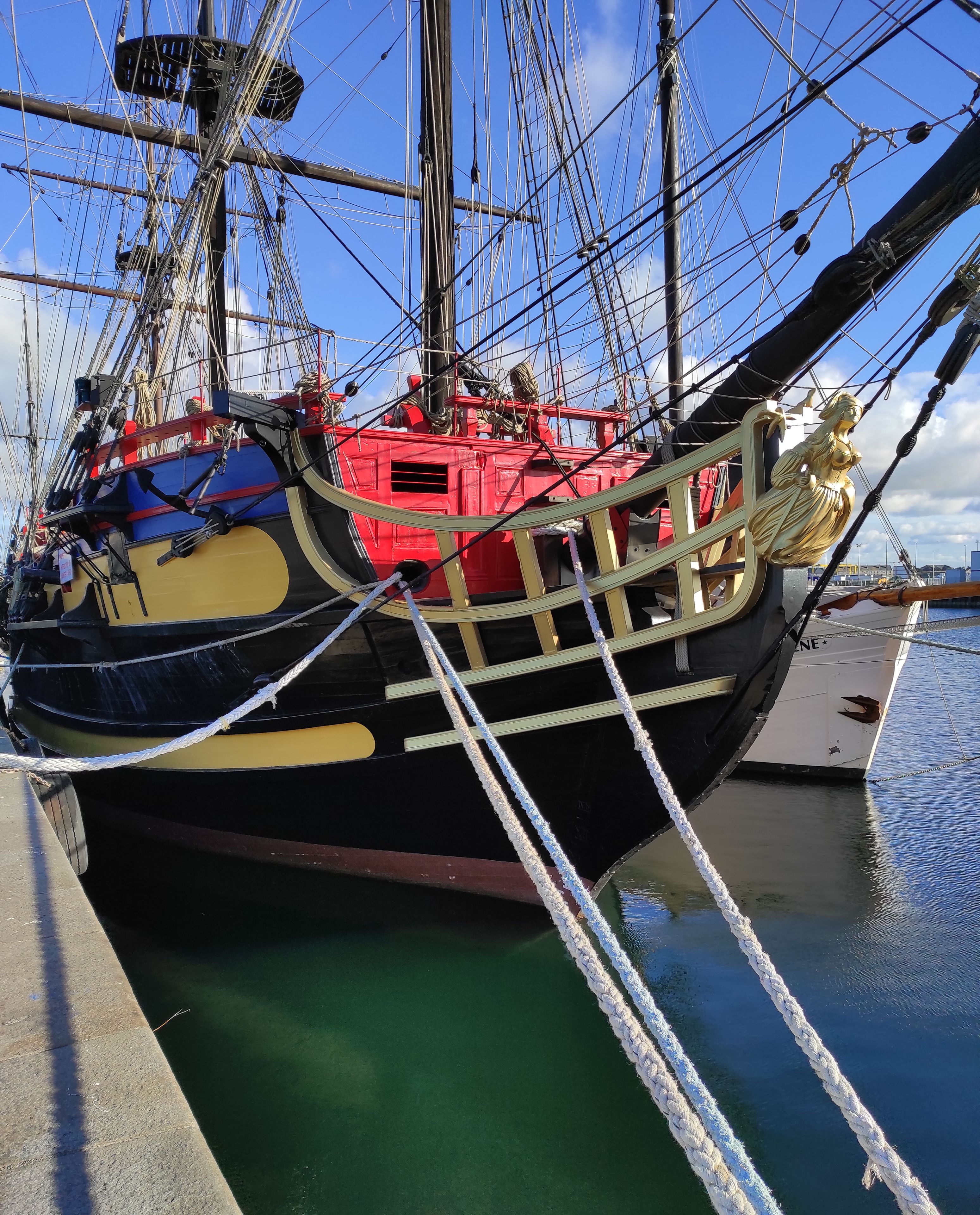 A large ship docked at a harbor with visible rigging and masts.