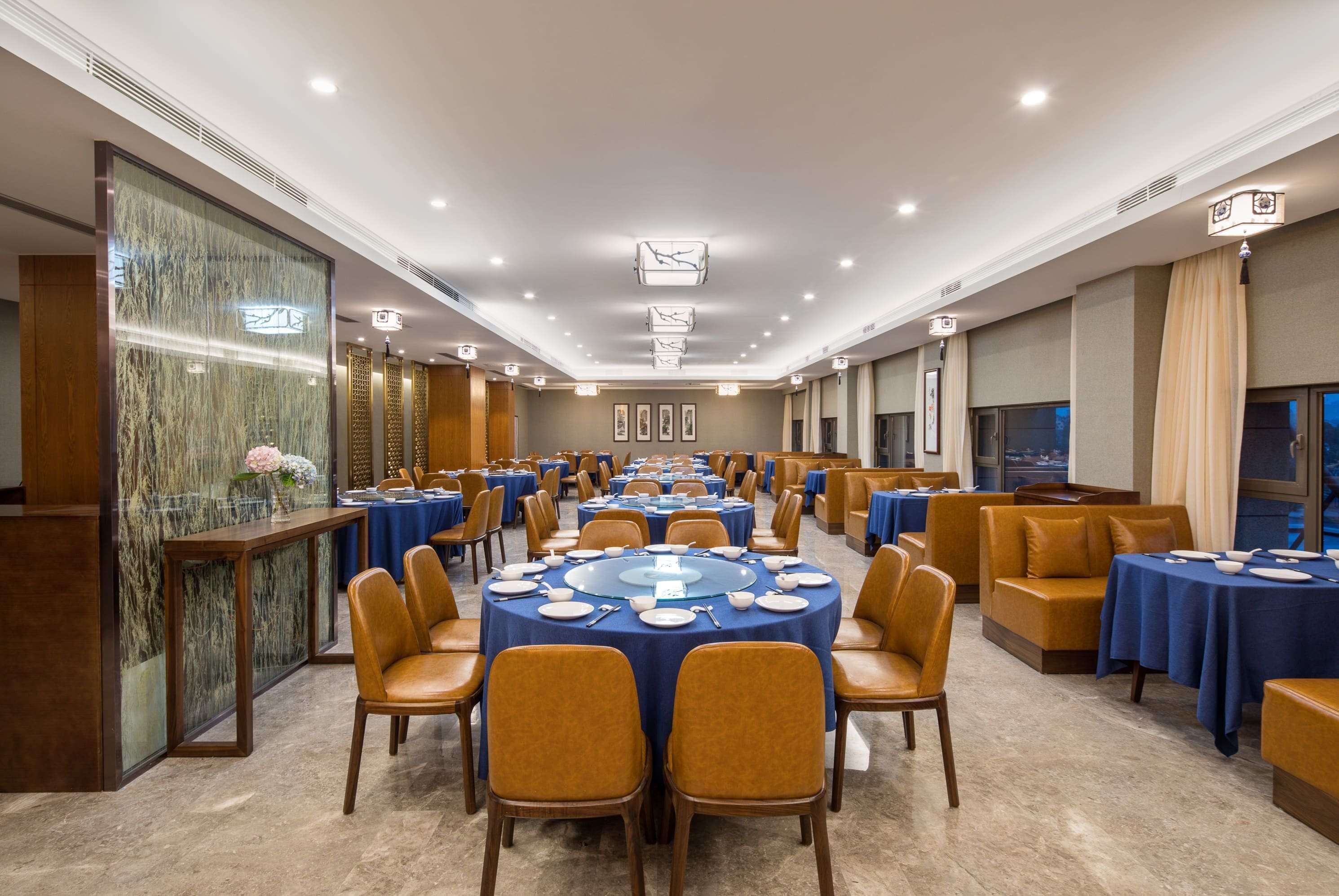 Una amplia sala de conferencias con mesas redondas, manteles azules y sillas anaranjadas.