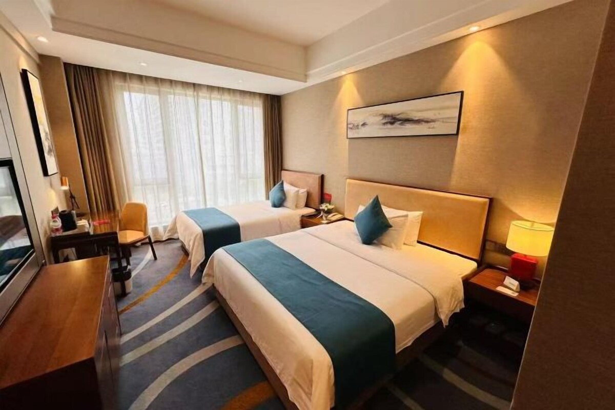 Habitación de hotel con dos camas, un escritorio, una silla, un televisor y una ventana con cortinas.
