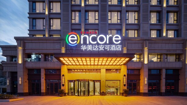 A multi-story hotel with a modern facade, featuring a prominent entrance with glass doors and a covered walkway. - Ramada Encore by Wyndham Wuhan Caidian (Wuhan)