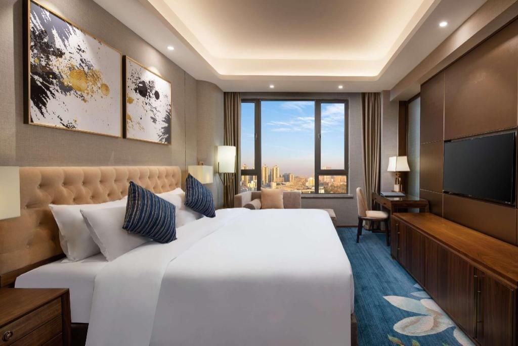 Quarto de hotel com uma cama grande, televisão, escrivaninha e vista da cidade.
