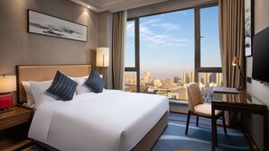 A hotel room with a large bed, a desk, a chair, a TV, and a city view. - Ramada Encore by Wyndham Wuhan Caidian (Wuhan)