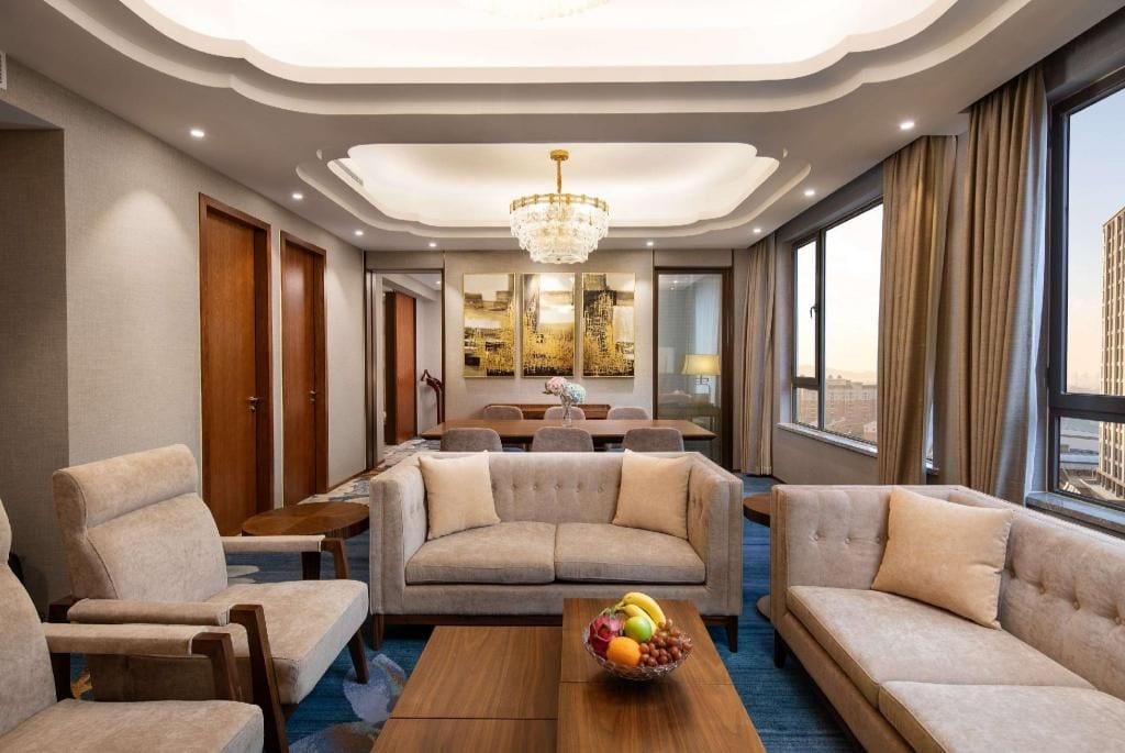 A hotel room with a sofa set, a dining table, and a chandelier.