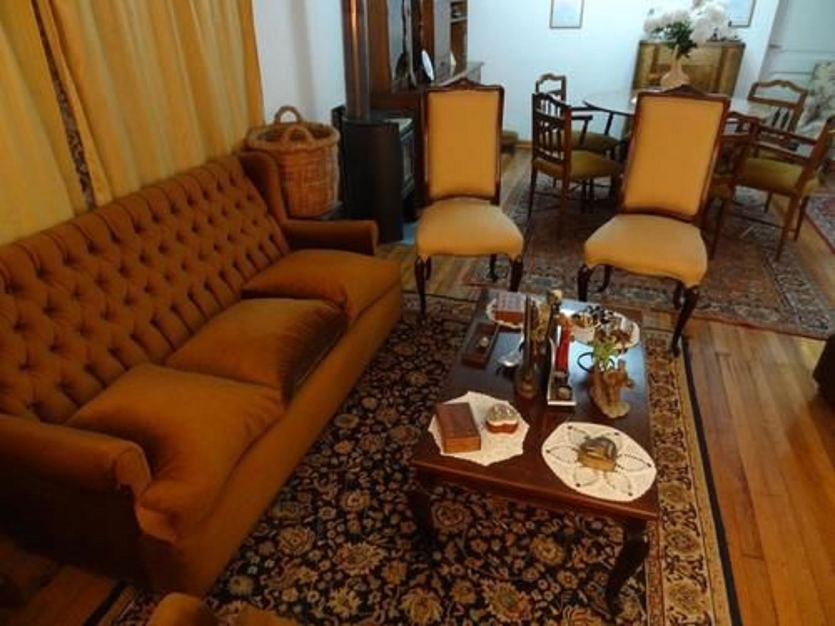 A traditional living room with a tufted sofa, two armchairs, a coffee table with decorative items, and a patterned rug.