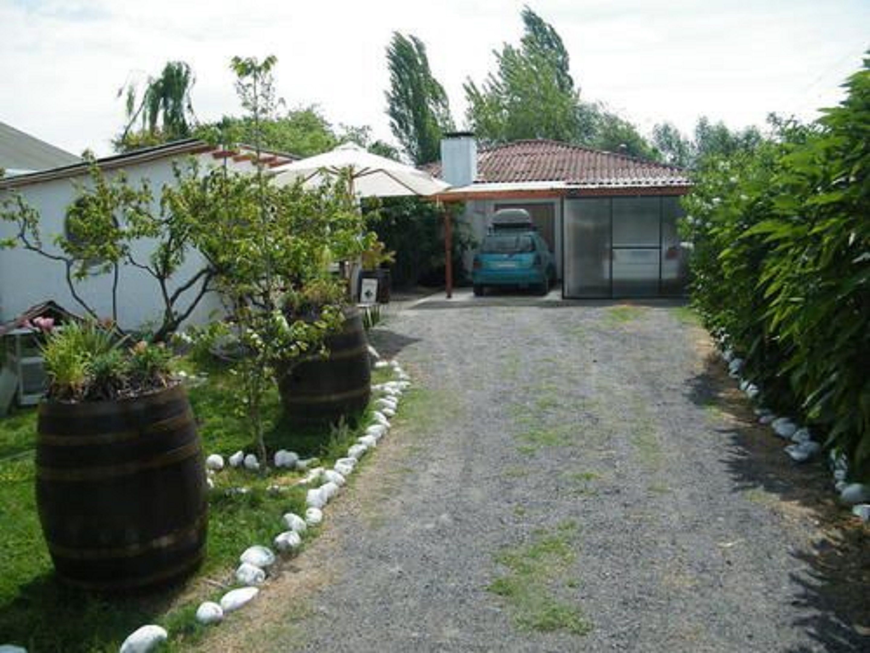 A gravel driveway leading to a house with a tiled roof, surrounded by greenery and potted plants.