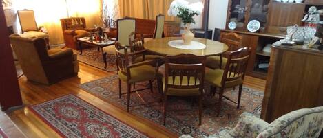 Una sala de estar con una mesa redonda de madera rodeada de sillas, un sofá y una alfombra estampada.