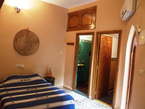 A bedroom with a bed, a wall-mounted lamp, a door leading to a bathroom, and a small heater. - Magnificent large Riad with swimming pool in the medina of Taroudant (Taroudant)