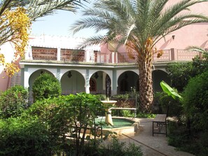 A courtyard with a fountain, palm trees, and a building with arches and balconies. - Magnificent large Riad with swimming pool in the medina of Taroudant (Taroudant)