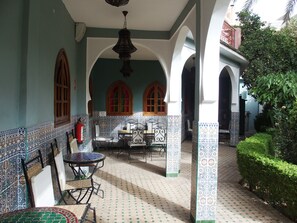 A covered outdoor seating area with patterned tiles, a fire extinguisher, and a view of the garden. - Magnificent large Riad with swimming pool in the medina of Taroudant (Taroudant)