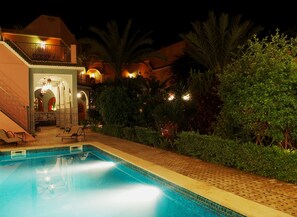 A nighttime view of a hotel with a swimming pool, outdoor seating, and a well-lit entrance. - Magnificent large Riad with swimming pool in the medina of Taroudant (Taroudant)