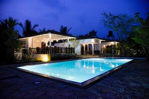 A nighttime view of a pool area with a house in the background, surrounded by palm trees and a stone pathway. - Odailem Resort (Unawatuna)