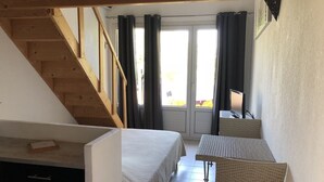 A bedroom with a bed, a desk, and a chair. There is a window with curtains and a view of the outside. - studio 2/3 people with porto vecchio pool (Porto-Vecchio)