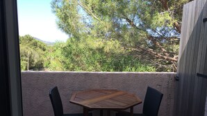 A balcony with a wooden table and two chairs, overlooking a garden with trees and a view of the hills. - studio 2/3 people with porto vecchio pool (Porto-Vecchio)