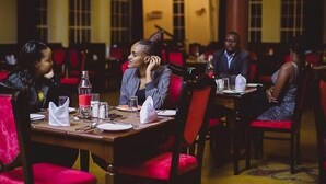 A dining area with tables set for four, red upholstered chairs, and a warm ambient lighting. - Tafaria Castle (Ndaragwa)