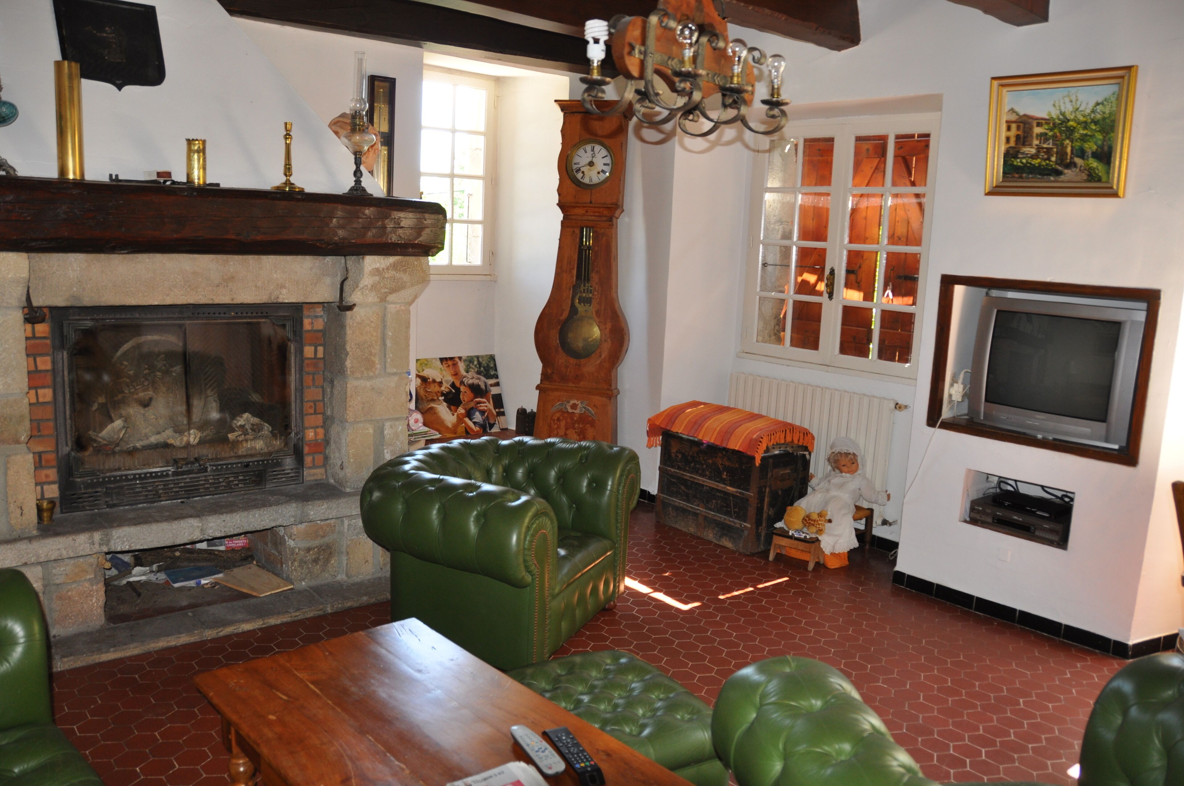 Una sala de estar con chimenea, sofás de cuero verde, una mesa de centro de madera, un reloj grande y un televisor.