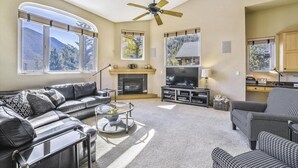 A spacious living room with a fireplace, a large TV, and a ceiling fan. - Larson Lane 217 - 4 Br Home (Frisco)