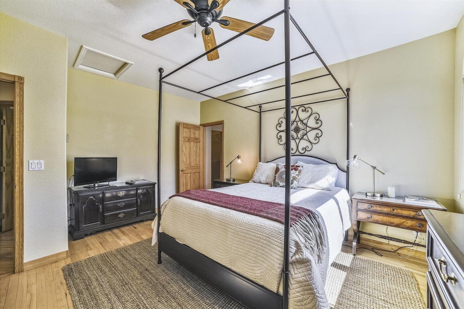 Une chambre à coucher avec un lit à baldaquin, un ventilateur de plafond, une télévision et un bureau avec une lampe.