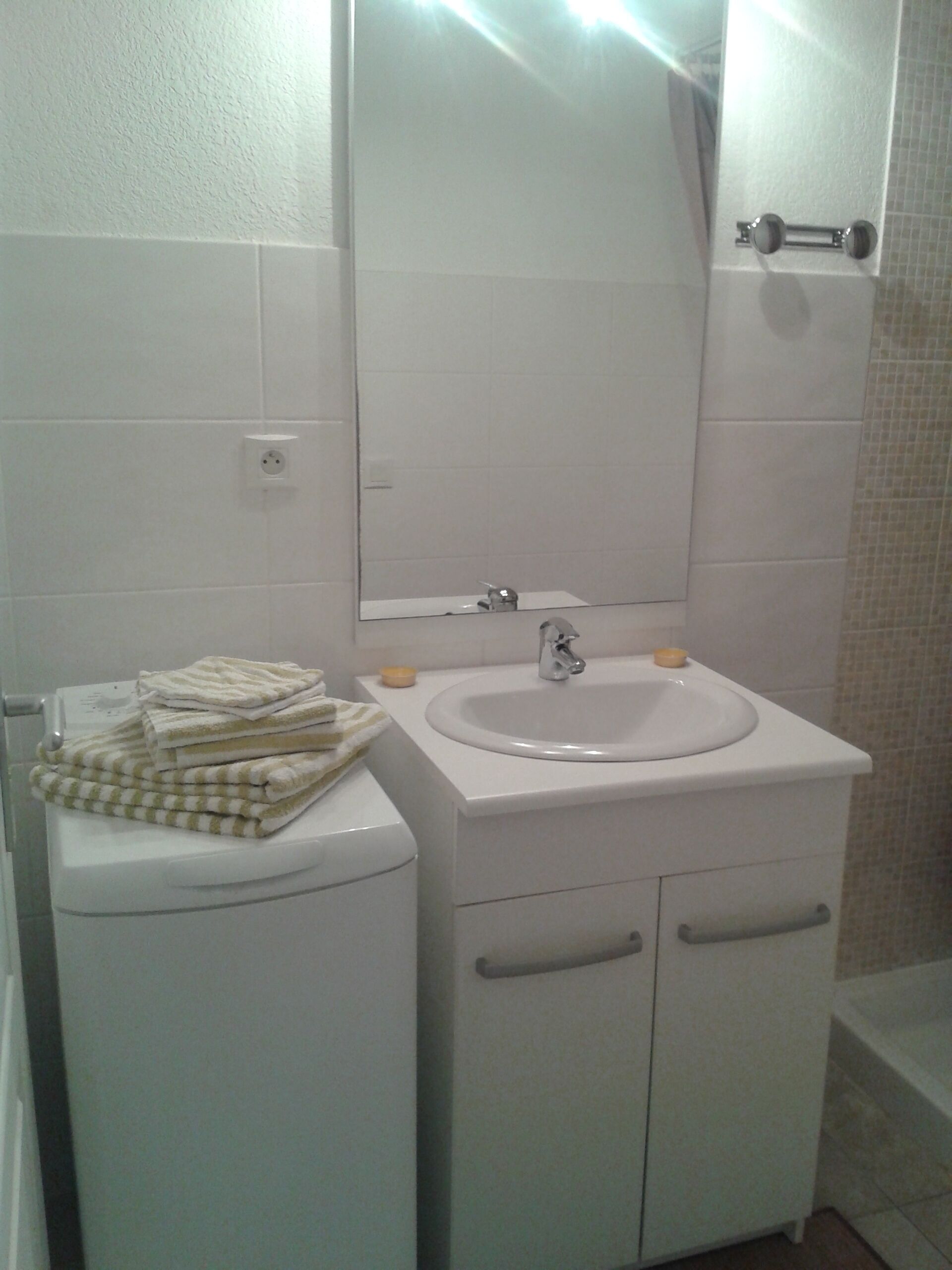Un baño con un lavamanos blanco, un espejo y un inodoro. Hay toallas apiladas sobre el inodoro.