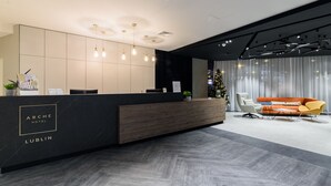 A modern hotel reception area with a black reception desk, wooden paneling, and a seating area with an orange sofa and a yellow chair. - Arche Hotel Lublin (Lublin)