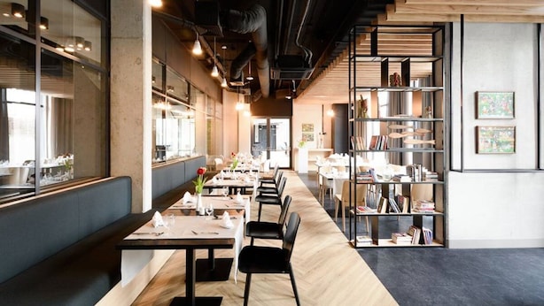 A modern restaurant with long tables, black chairs, and a bookshelf on the right. - Arche Hotel Lublin (Lublin)