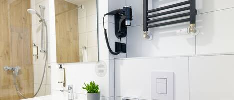 Un baño moderno con un lavamanos blanco, un inodoro, un perchero para toallas, un espejo, una toalla, una planta en maceta, un toallero y una ducha con puerta de cristal.