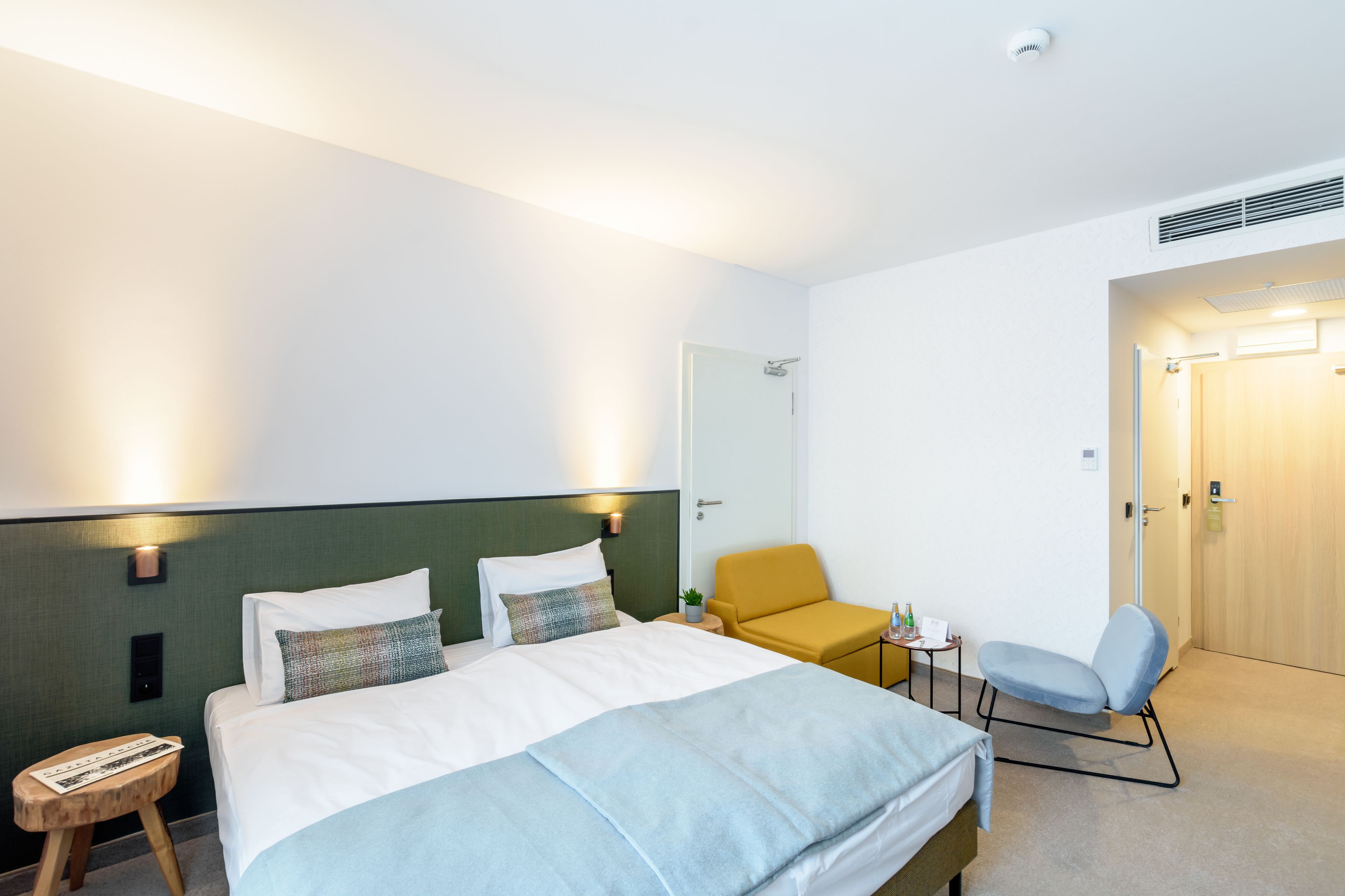 Una habitación de hotel con una cama, una mesita pequeña con una silla y una puerta que da a otra habitación.