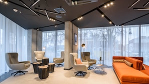 A modern interior with a large orange sofa, multiple armchairs, and a coffee table. - Arche Hotel Lublin (Lublin)