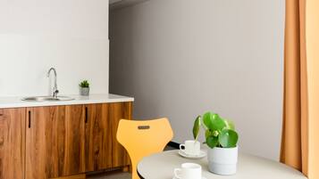A modern kitchen with wooden cabinets, a white countertop, and a sink. There is a dining area with a round table and two yellow chairs. A potted plant is on the table.