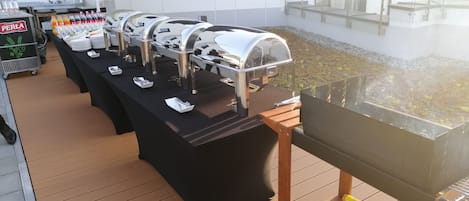 Montaje de bufé con varias parrillas y estaciones de servicio en una terraza al aire libre.