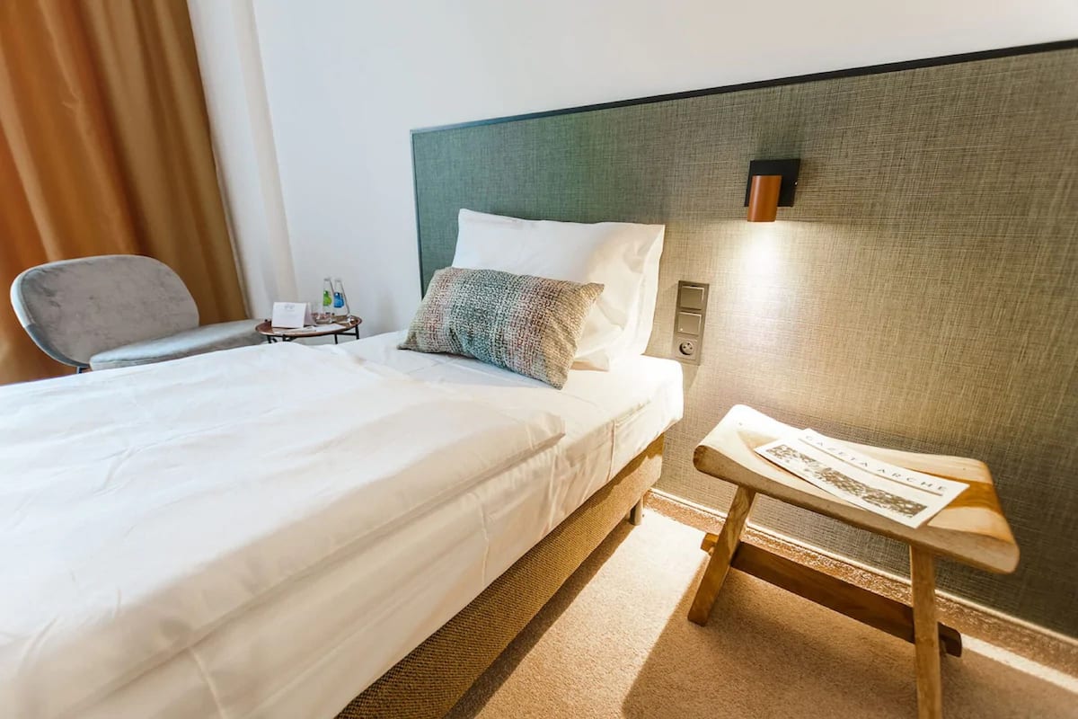 A hotel room with a neatly made bed, a small bedside table with a lamp, and a chair.