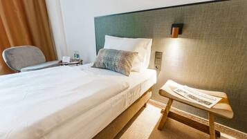 Una habitación de hotel con una cama bien hecha, una mesita de noche con una lámpara y una silla.