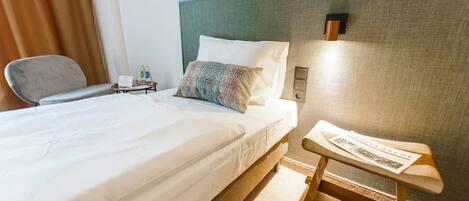 A hotel room with a neatly made bed, a small bedside table with a lamp, and a chair.