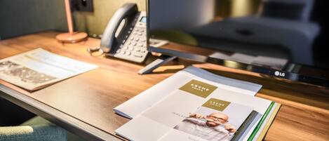A hotel room desk with a telephone, a laptop, and brochures.