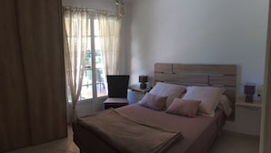 A bedroom with a bed, curtains, a bedside table, a lamp, and a window.