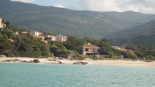 A coastal area with houses on a hillside, a beach, and a view of the sea.