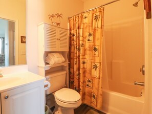 Een badkamer met een toilet, een wastafel, een kast en een douchegordijn met een palmboommotief.