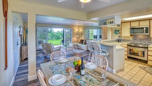 Une cuisine spacieuse dotée d’appareils électroménagers modernes, un coin repas avec des meubles en osier et de grandes fenêtres offrant une vue sur l’extérieur.