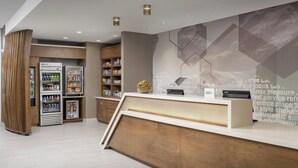 Un espace d’accueil moderne, doté d’un comptoir de réception en bois, d’un réfrigérateur rempli de boissons et d’un mur orné de motifs géométriques abstraits.