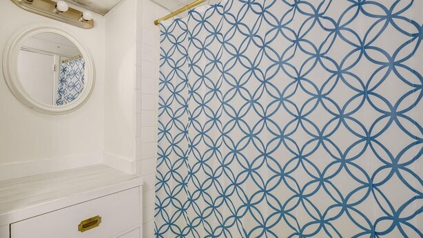 Ein Badezimmer mit einem weißen Waschtisch, einem goldenen Wasserhahn und einem blauen, geometrisch gemusterten Duschvorhang.