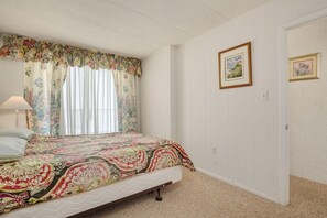 A bedroom with a bed, floral curtains, a lamp, and two framed pictures on the wall.