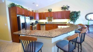 A kitchen with granite countertops, wooden cabinets, a refrigerator, stove, and a dining area with bar stools.