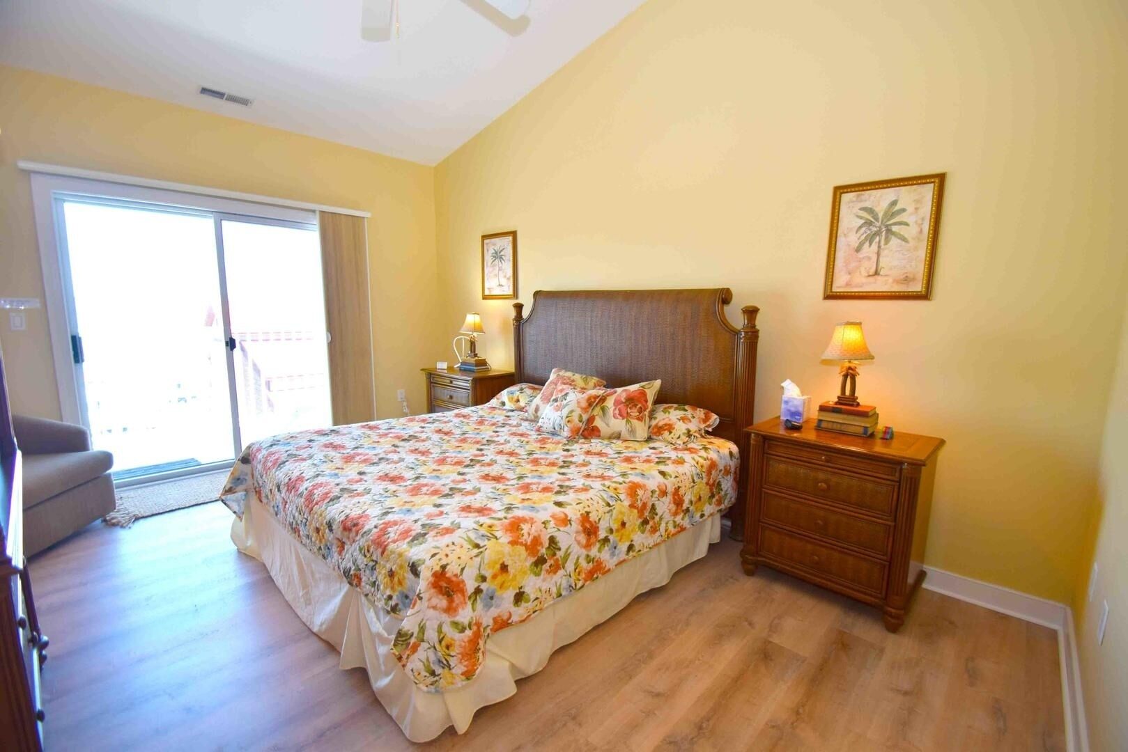 Une chambre à coucher comprenant un lit, une table de chevet, une chaise et une porte-fenêtre coulissante donnant sur un balcon.