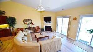A living room with a sectional sofa, a fireplace, a television, and a sliding glass door to the outside.
