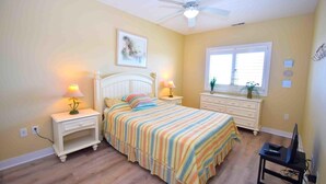 A bedroom with a bed, bedside tables, a ceiling fan, a window, and a TV stand.