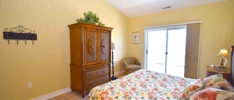 A bedroom with a floral bedspread, a wooden cabinet, a ceiling fan, and a chair near a sliding glass door.